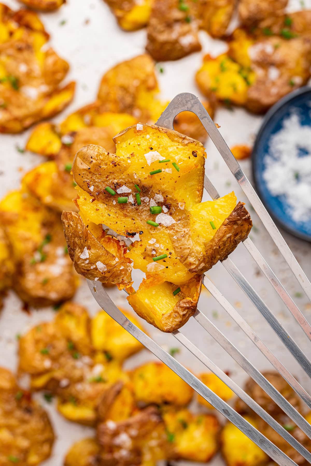 A smashed potato topped with salt and fresh chives on a metal spatula.
