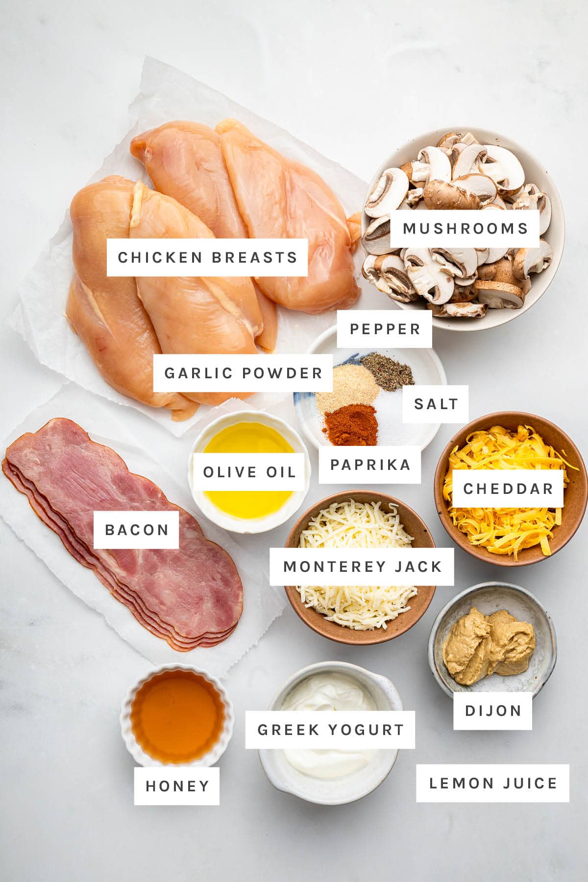Ingredients measured out to make Alice Springs Chicken: chicken, mushrooms, garlic powder, pepper, salt, paprika, olive oil, cheddar, Monterey jack, bacon, honey, Greek yogurt, dijon and lemon juice.
