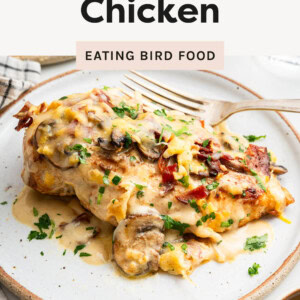 Cheesy chicken on a plate, topped with mushrooms and bacon.