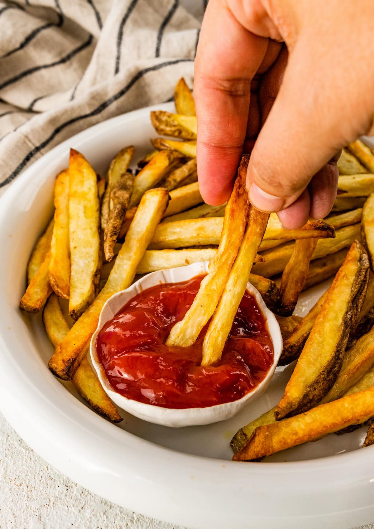 A woman's hand dips french fries into ketchup.