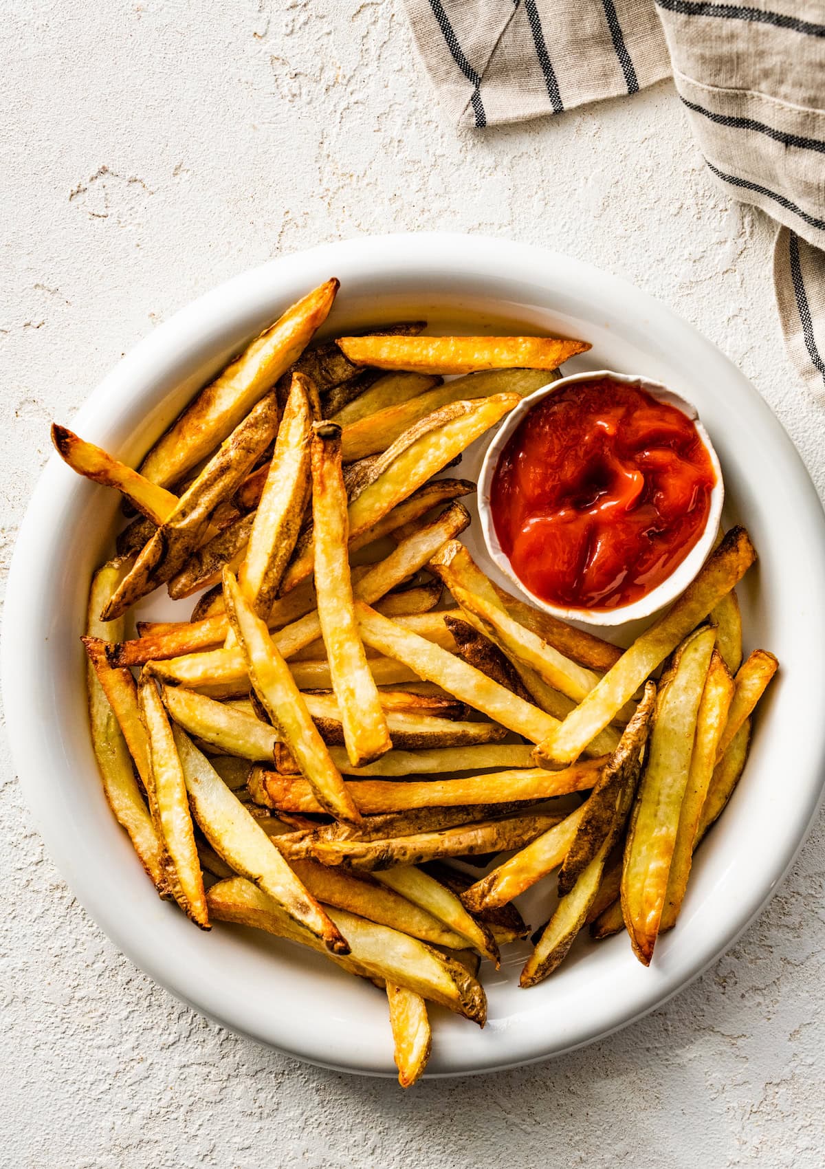 A plate of air fryer french fries with a small container of ketchup on the side.