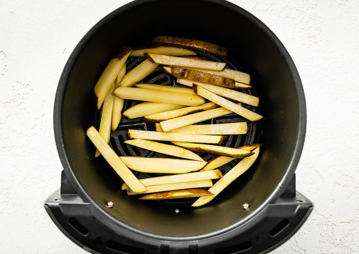 An air fryer basket with un-cooked french fries.