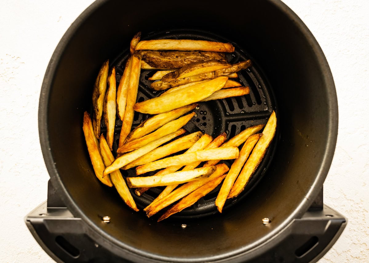 An air fryer basket with french fires.