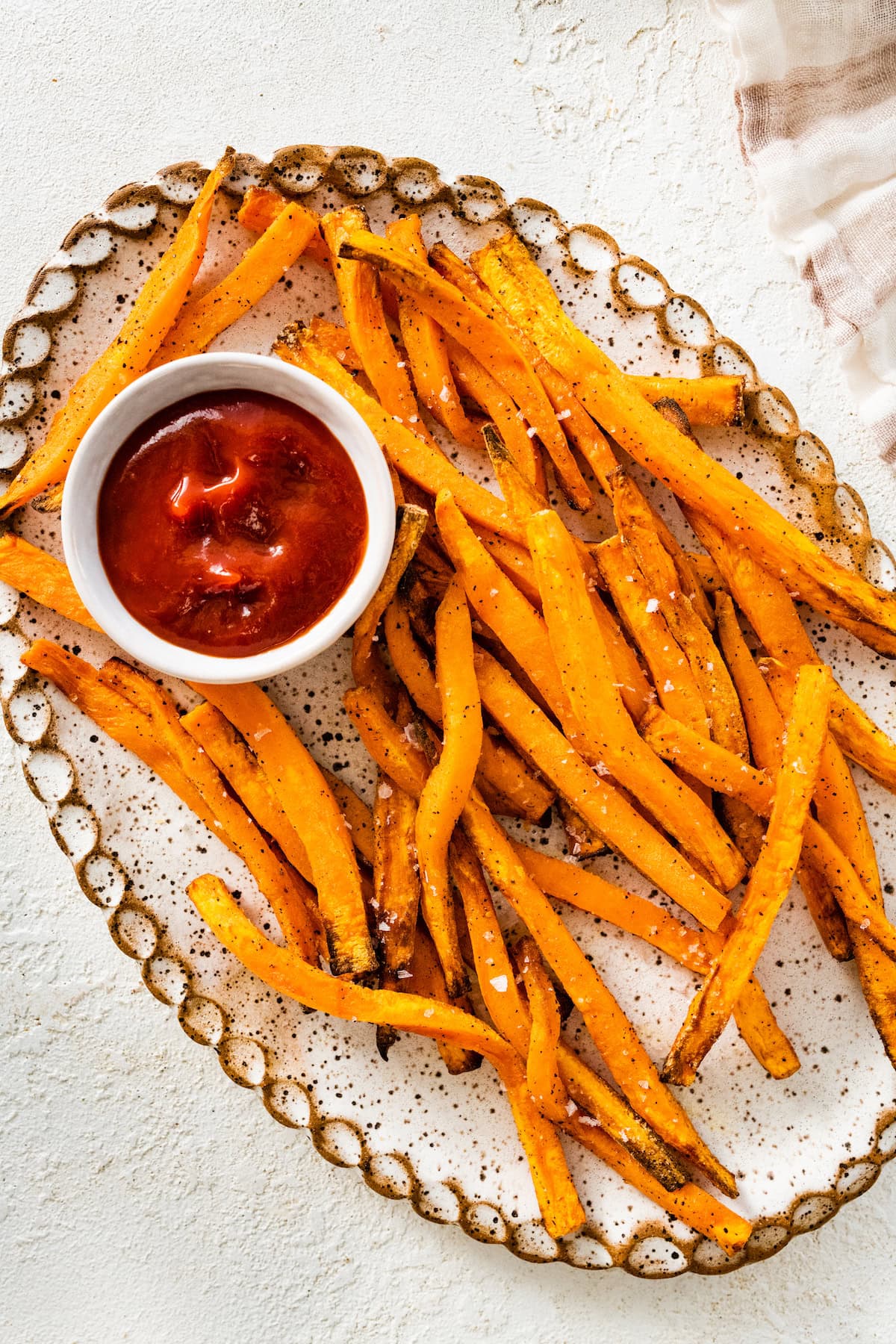 An overhead image of sweet potato fries on a white tray served alongside a small white bowl of ketchup.