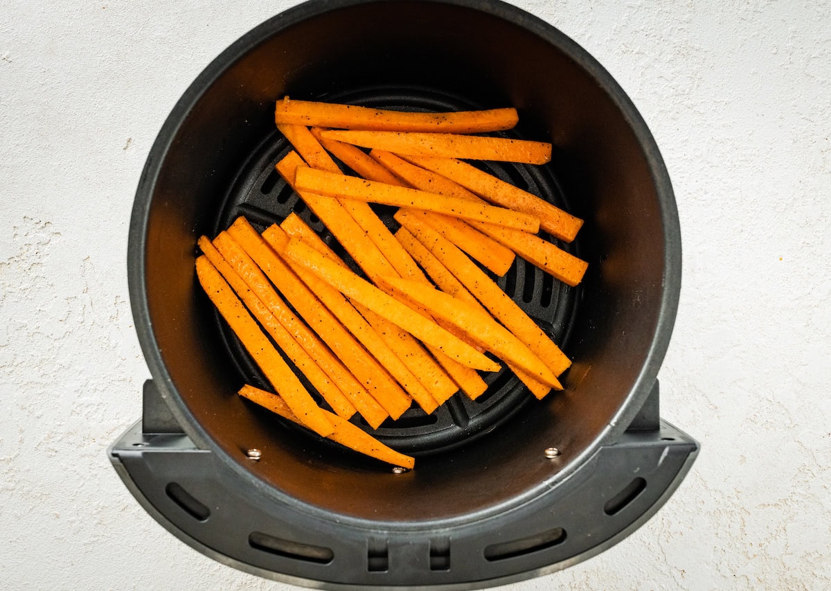 Sweet potato fries in the basket of an air fryer before being cooked.