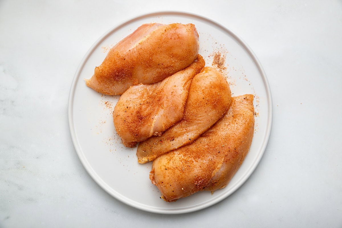 Four seasoned chicken breasts on a white plate.