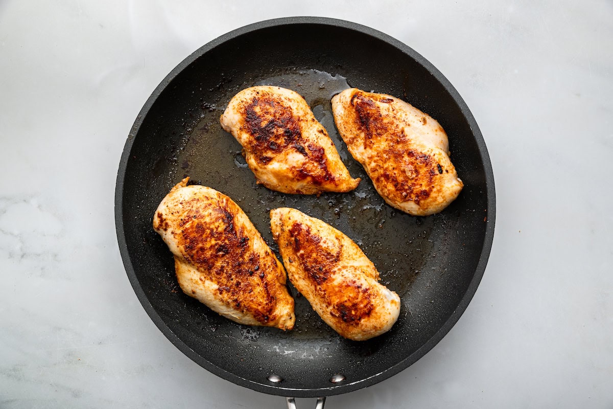 Four chicken breasts cooked in a skillet.