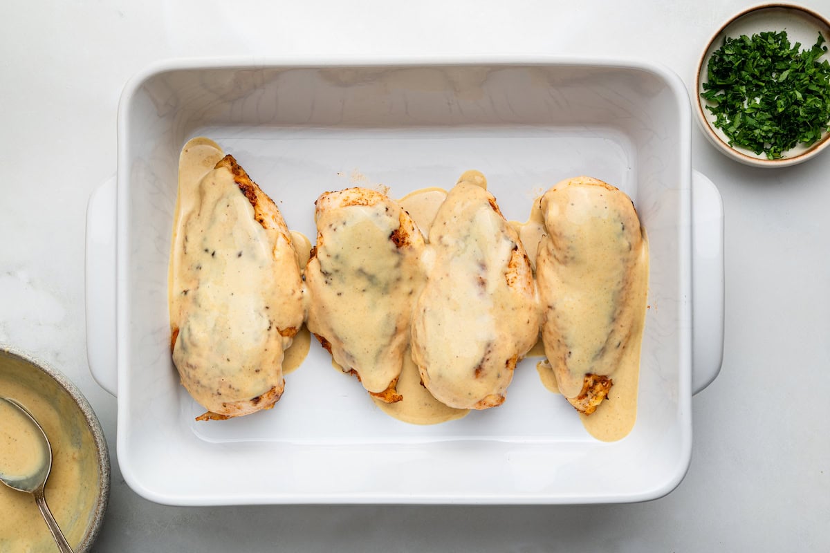 Four chicken breasts in a white baking dish topped with a honey mustard sauce.