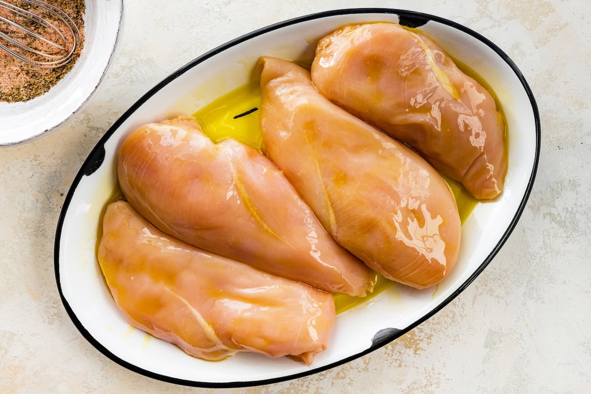 Four raw chicken breasts covered in olive oil in a large dish.