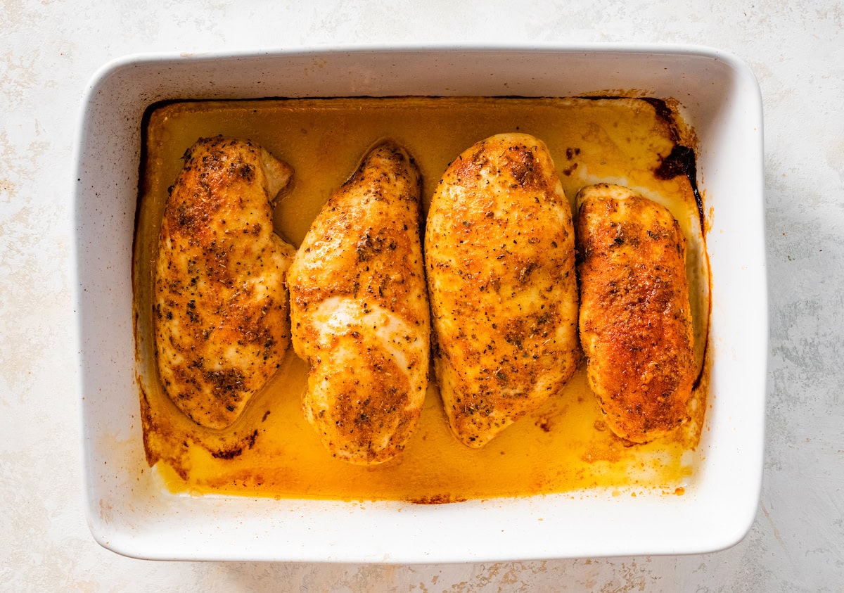 Four baked chicken breasts in a large baking dish.