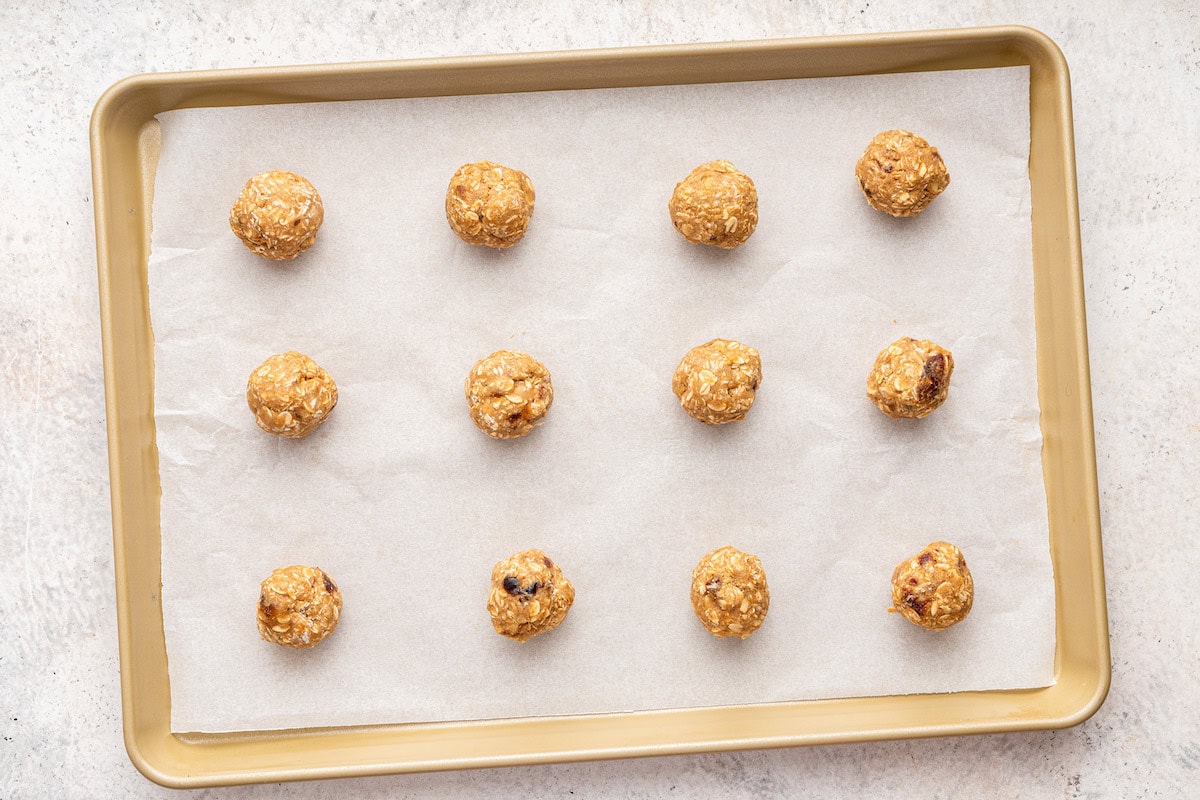 12 oatmeal date cookies dough balls lined up on a parchment-lined baking sheet.