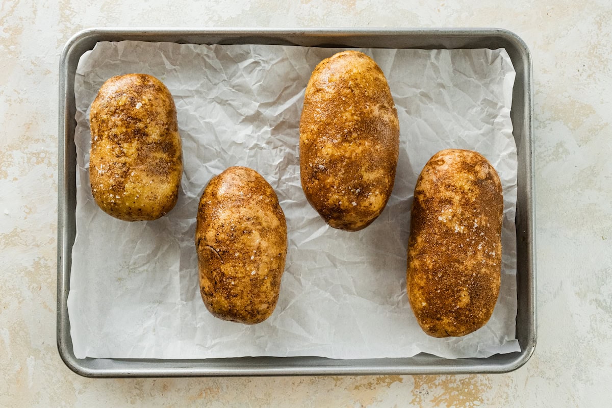 Four potatoes on a baking tray.
