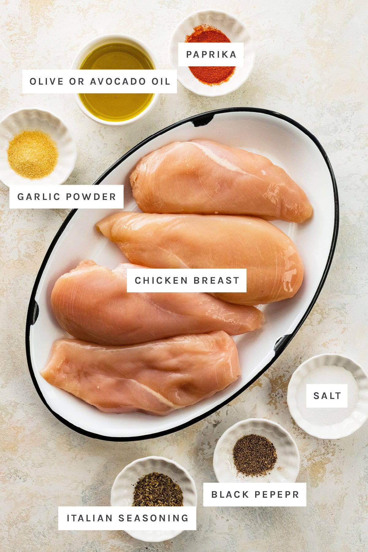 Ingredients measured out to make Baked Chicken Breast: garlic powder, olive oil, paprika, chicken breast, Italian seasoning, black pepper and salt.