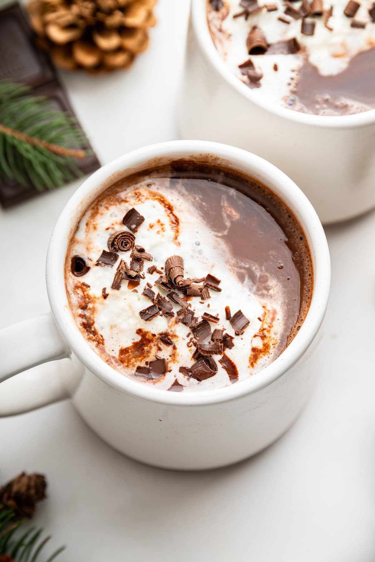 A white mug with hot chocolate with chocolate shavings and a touch of whipped cream.