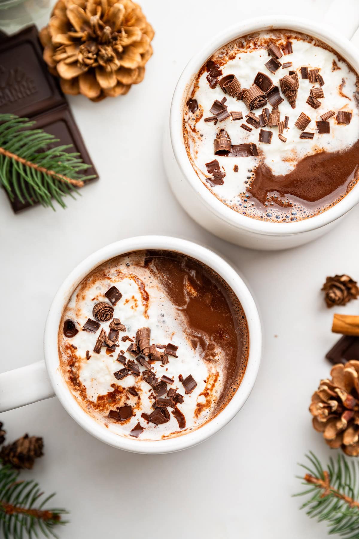 Two white mugs with hot chocolate that are each topped with whipped cream and chocolate shavings.