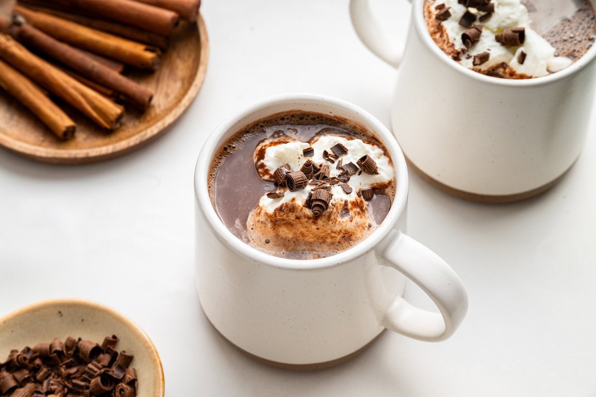 A white mug of hot chocolate topped with whipped cream and chocolate shavings.