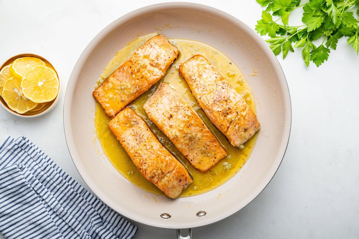 Four salmon filets in a pan with melted butter and garlic.