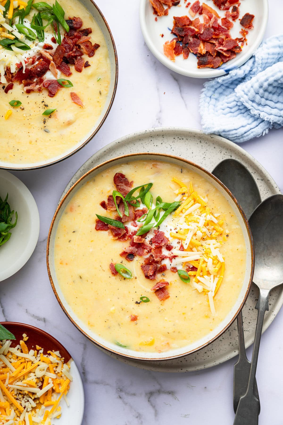 Two bowls of potato soup topped with bacon bits, green onion, shredded cheese and sour cream.