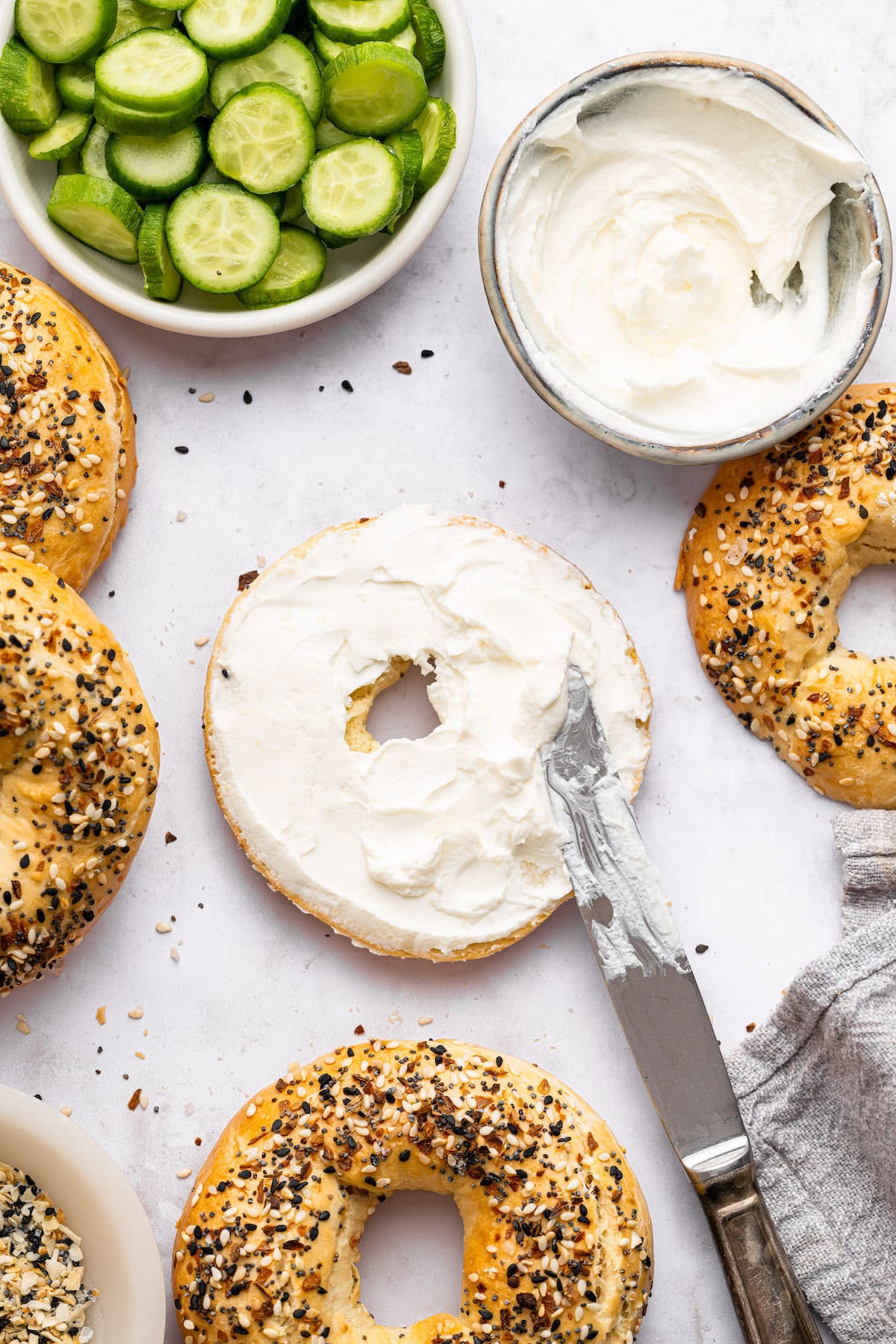 One sliced everything bagel with plain cream cheese on it that's been spread by a silver knife.