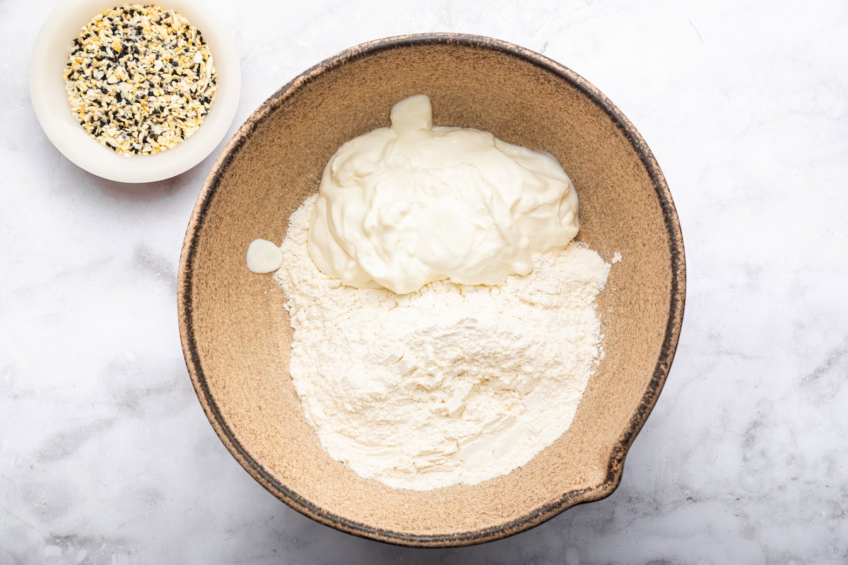A large brown mixing bowl with Greek yogurt and flour used to make a dough for protein bagels.