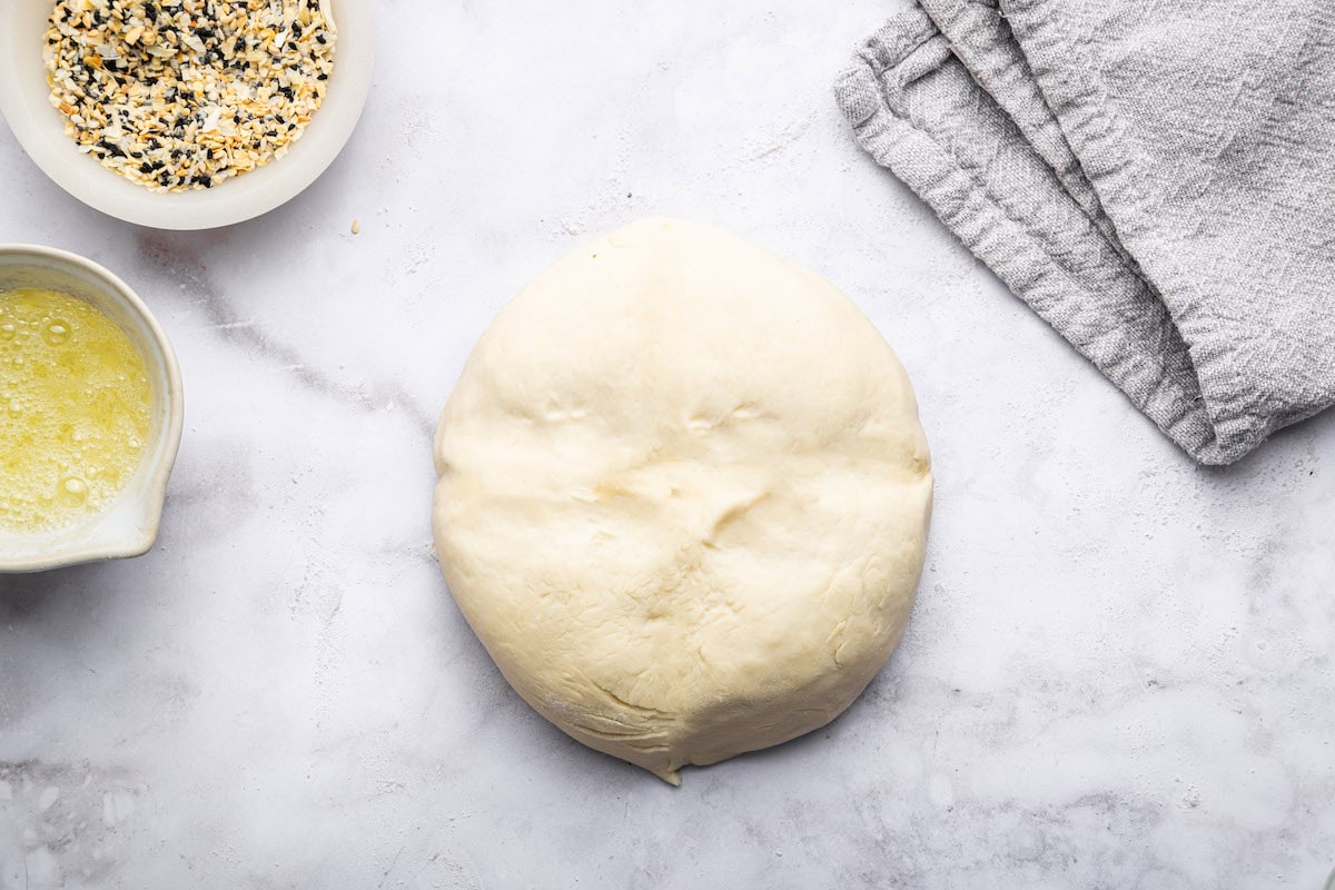 A large dough ball for protein bagels near two containers. One is egg whites and the other is everything bagel seasoning.
