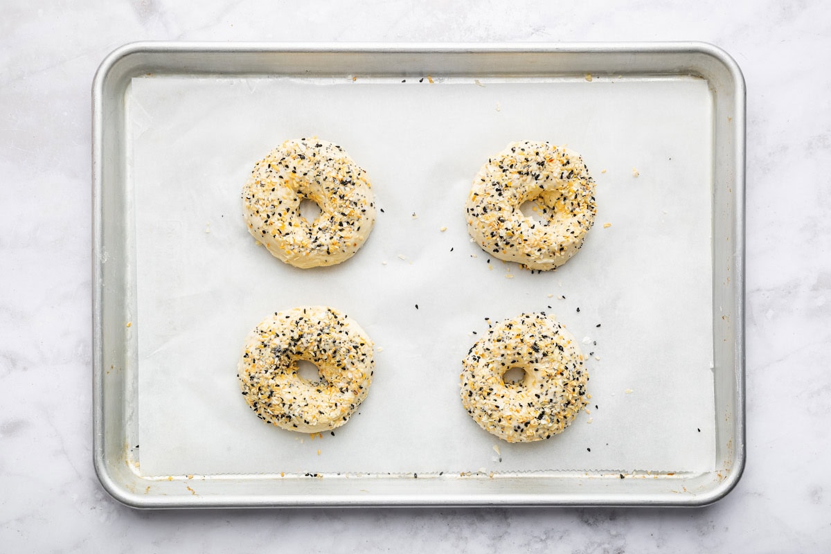 Four protein bagels topped with everything bagel seasoning on a baking tray before being baked in the oven.