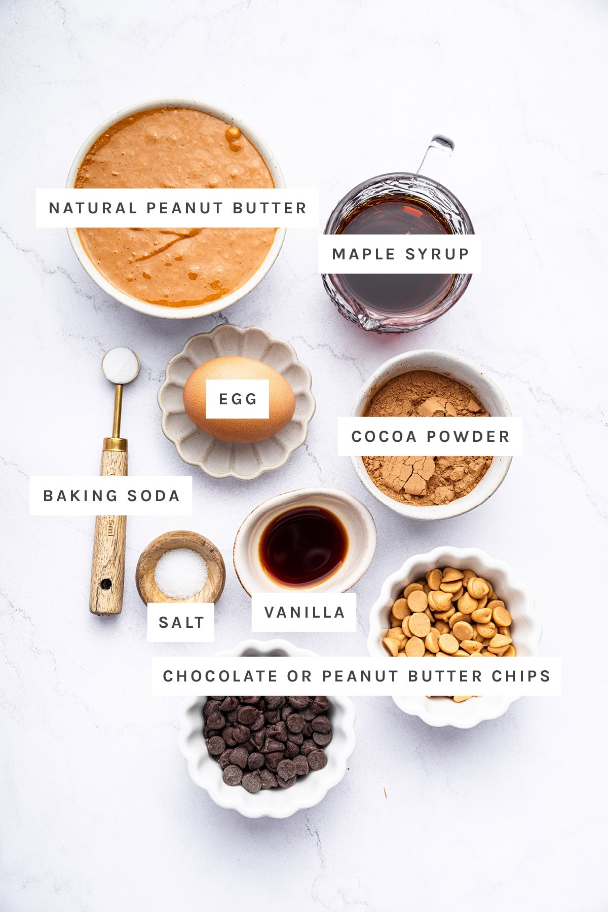 Ingredients measured out to make Chocolate Peanut Butter Cookies: natural peanut butter, maple syrup, egg, cocoa powder, baking soda, salt, vanilla, chocolate chips and peanut butter chips.