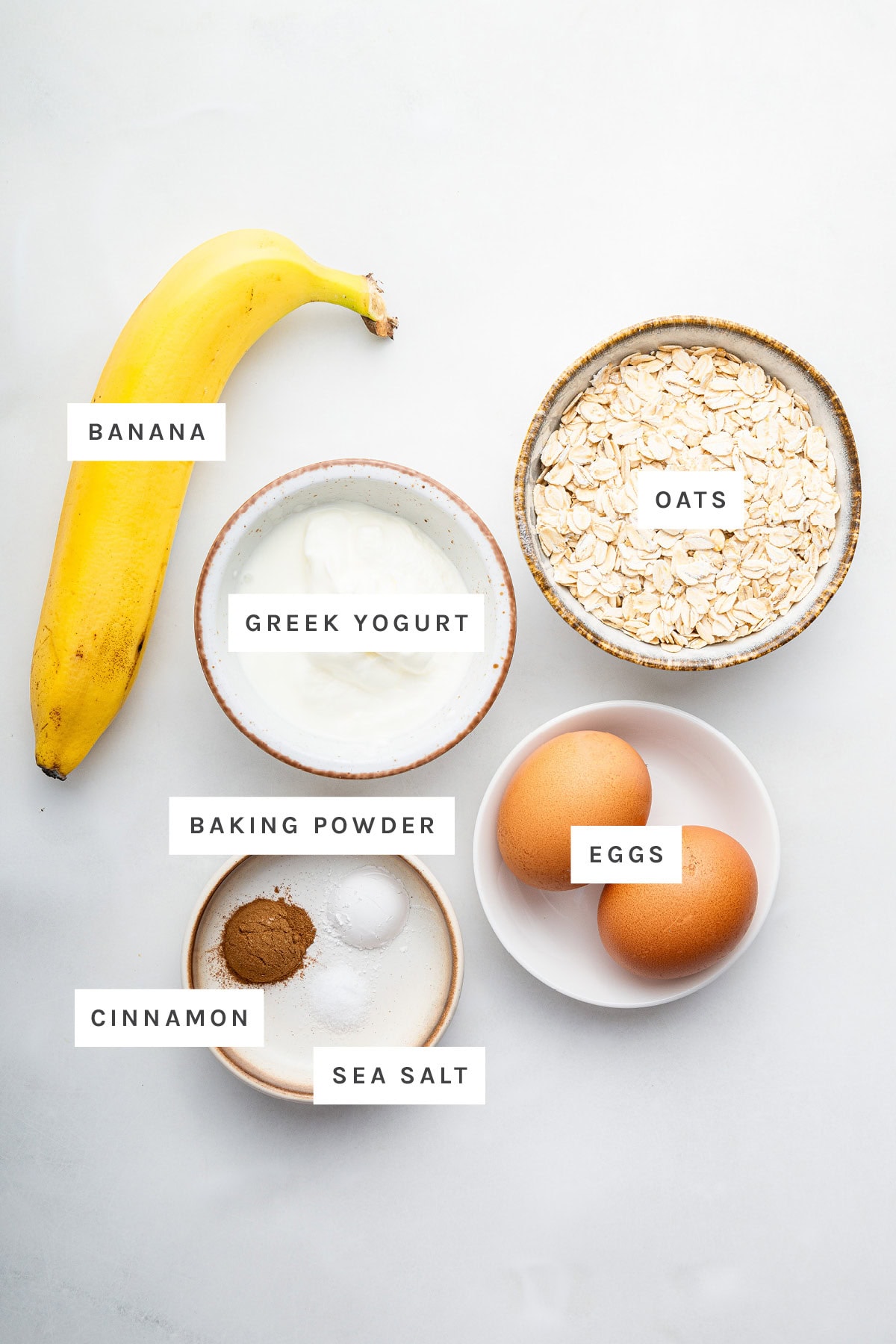 Ingredients measured out to make Greek Yogurt Pancakes: banana, Greek yogurt, oats, eggs, baking powder, cinnamon and sea salt.