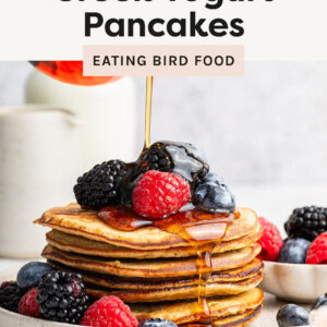 Maple syrup being poured over a stack of Greek Yogurt Pancakes served with berries.