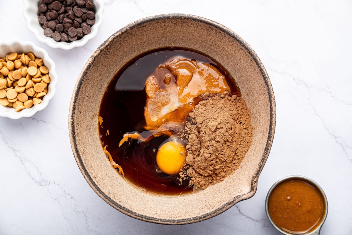 Ingredients to make the chocolate peanut butter cookies in a bowl: natural peanut butter, maple syrup, egg, cocoa powder, baking soda, salt and vanilla.