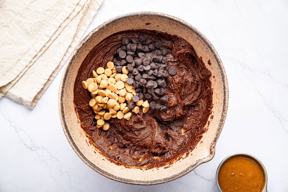 Chocolate chips and peanut butter chips added to the dough batter in a mixing bowl.