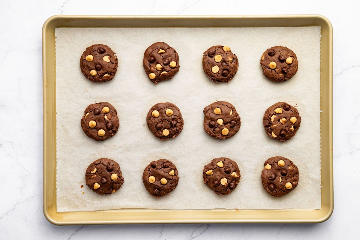 12 baked chocolate peanut butter cookies on a parchment-lined baking sheet.