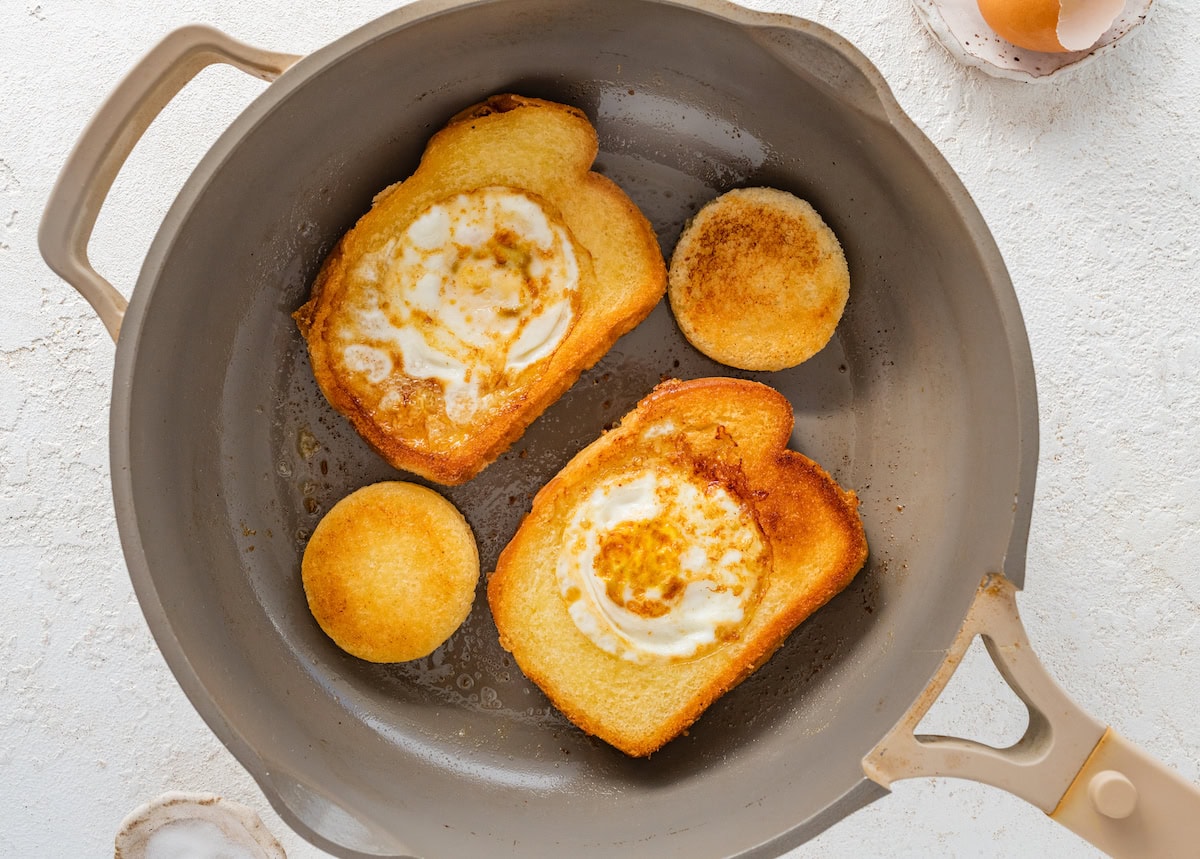 Two slices of toasted bread on a skillet each with a cooked egg in the center of them.