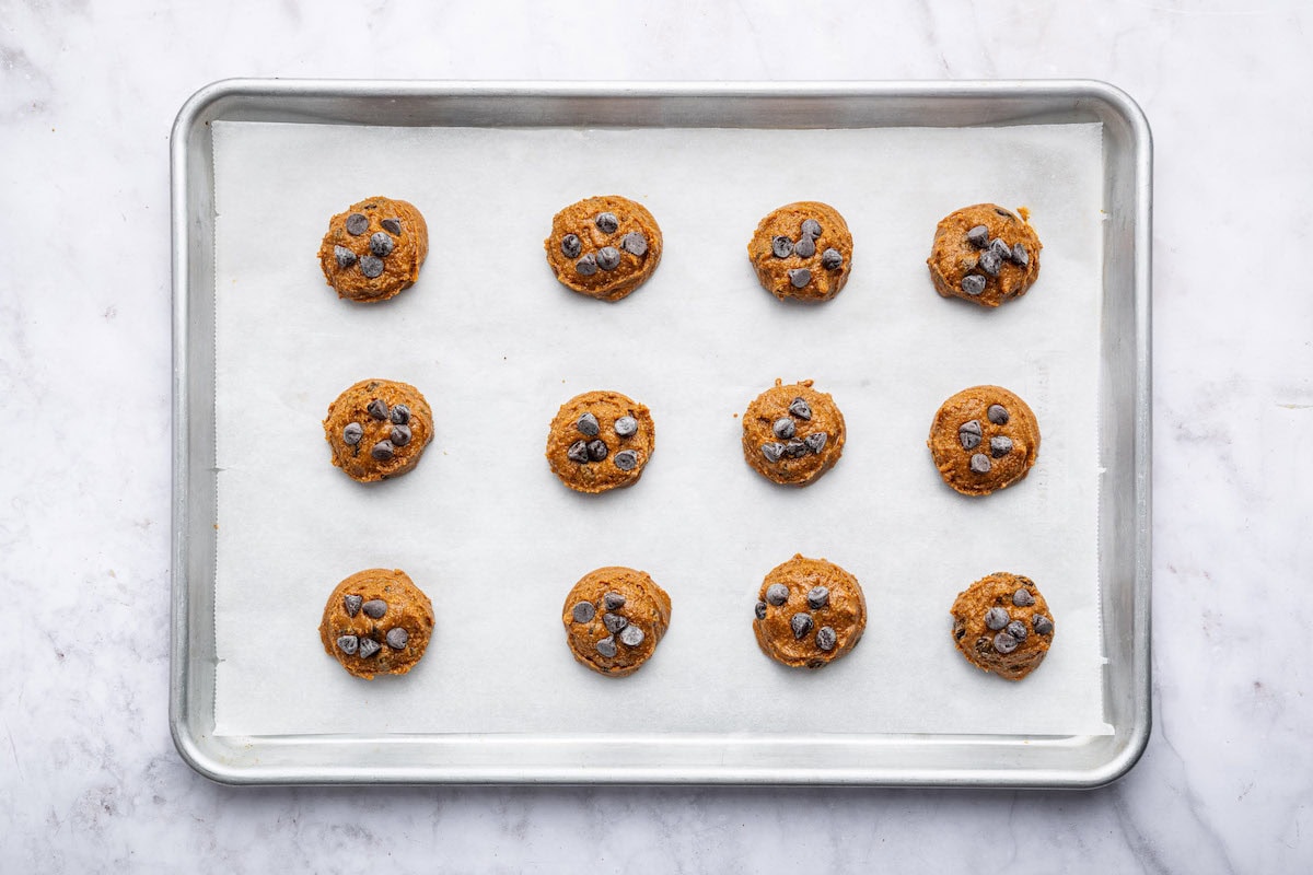 12 unbaked flourless peanut butter cookies with chocolate chips on a baking sheet lined with parchment paper.