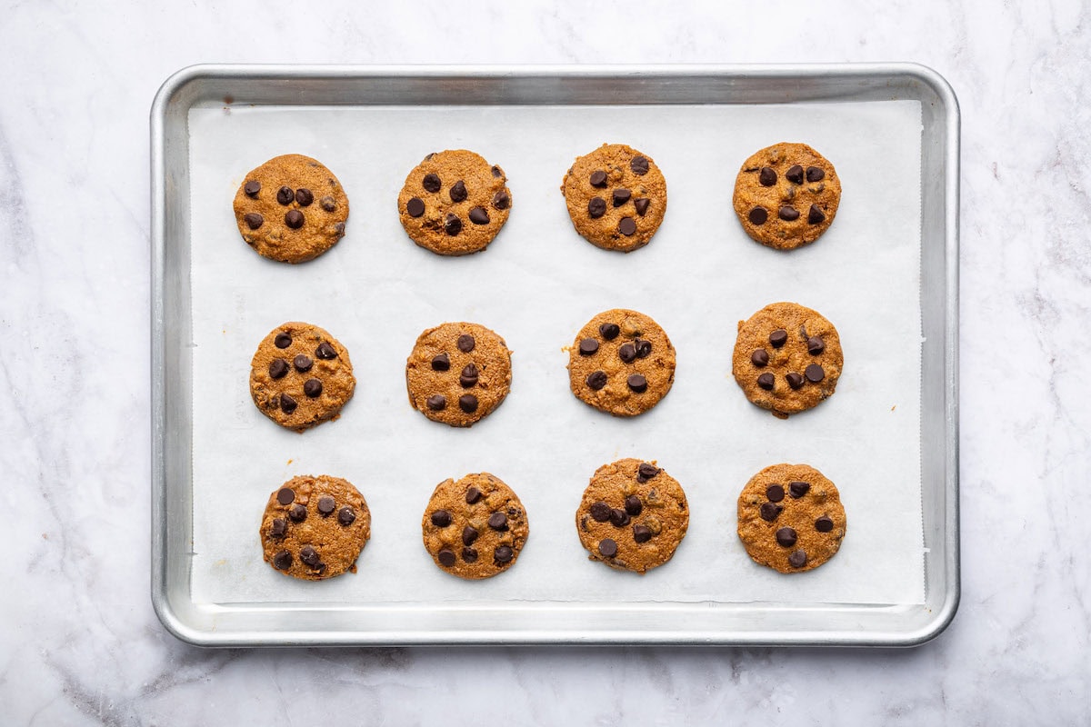 12 baked flourless peanut butter cookies with chocolate chips on a baking sheet lined with parchment paper.