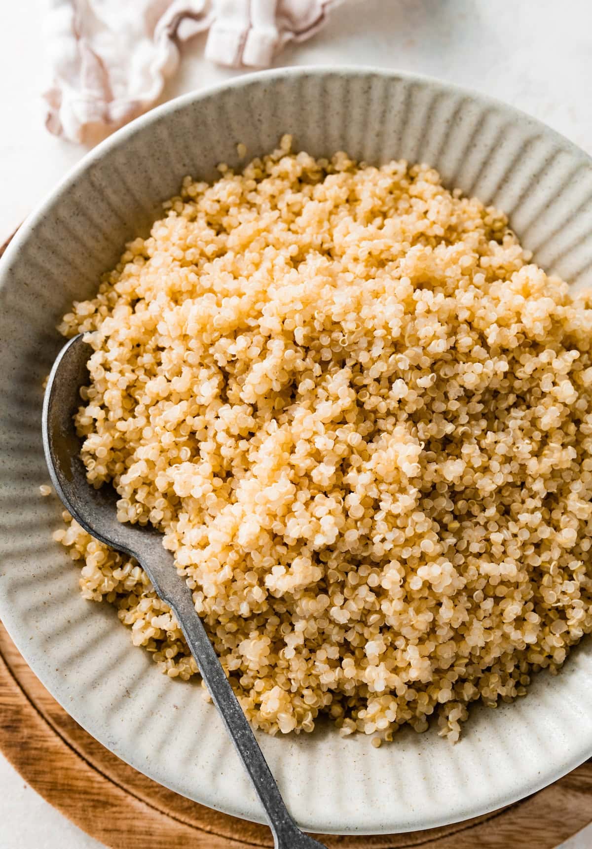 A bowl of cooked quinoa on a wooden cutting board. There is a silver spoon in the bowl of quinoa.