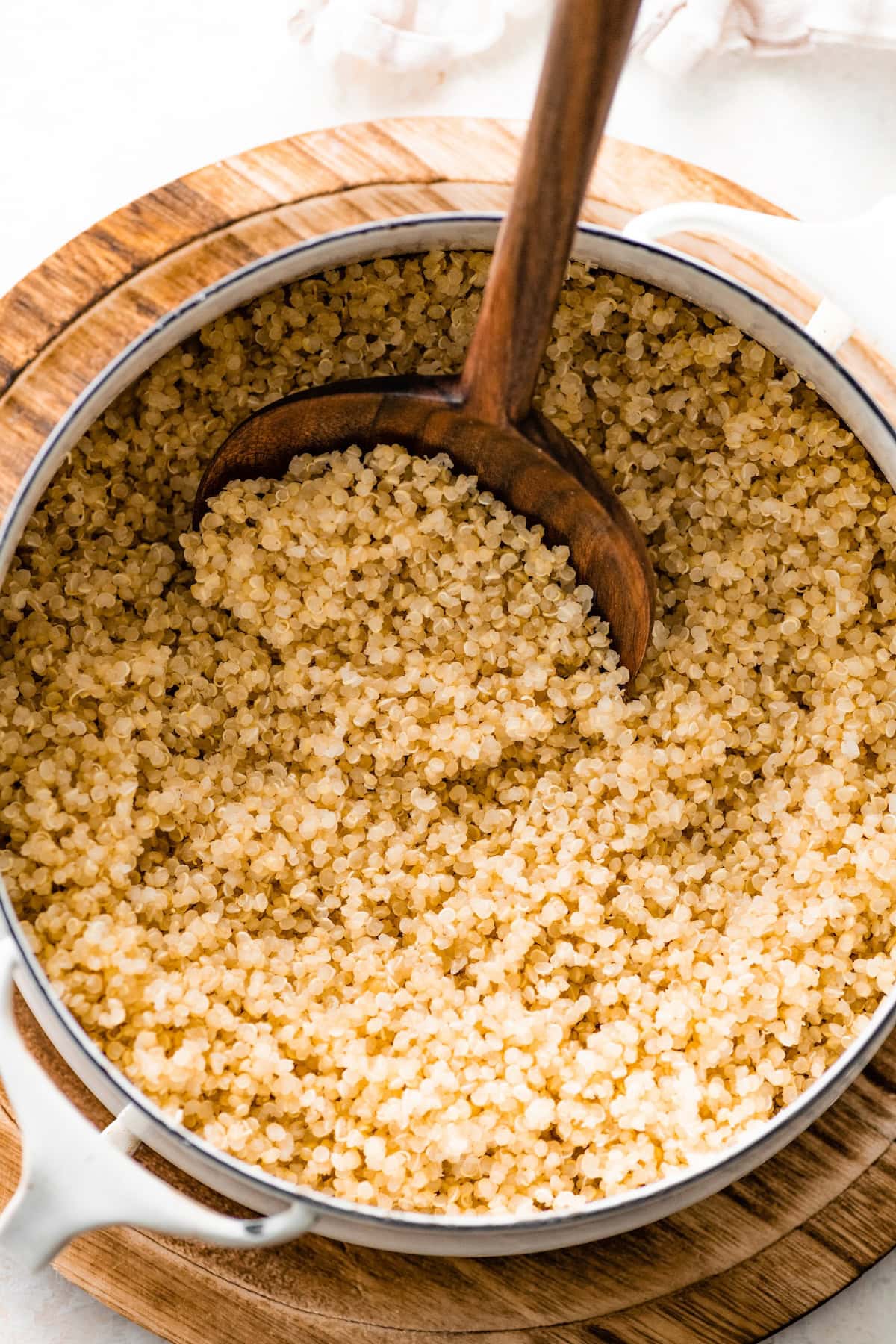 A large wooden spoon in a large white pot that is filled with cooked quinoa.