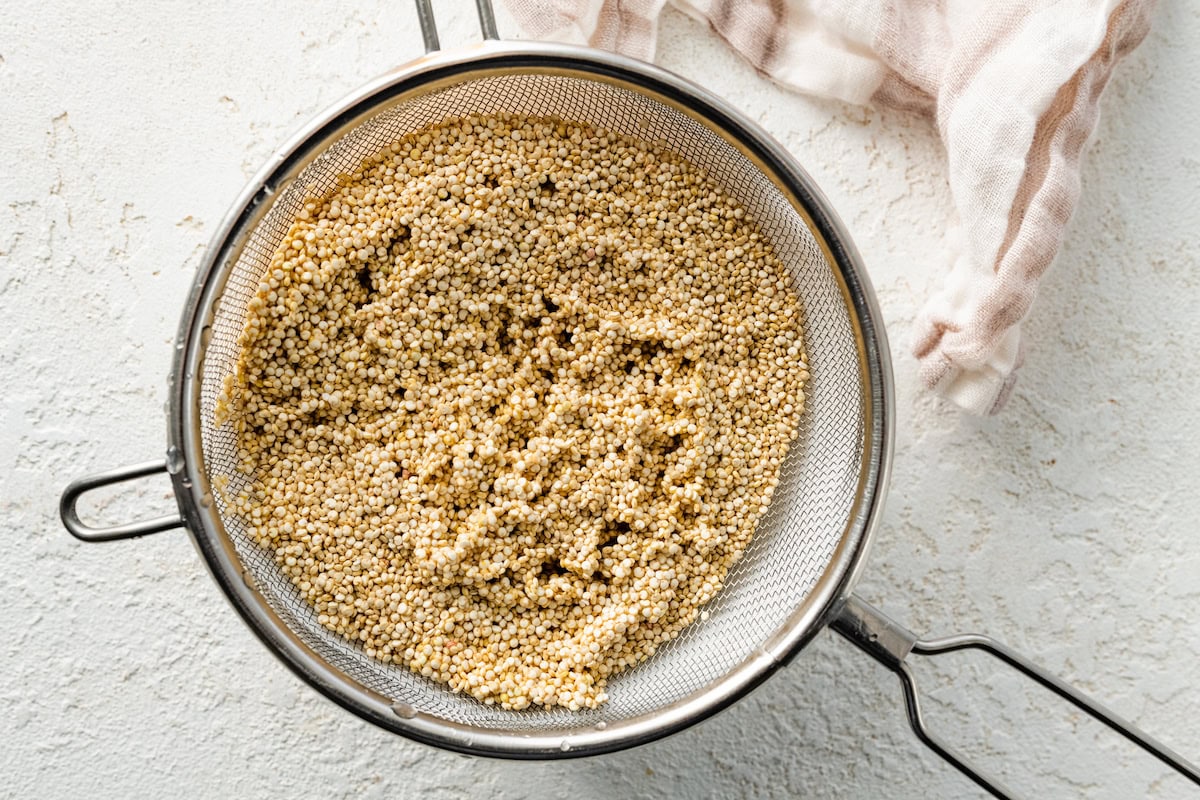A mesh strainer with uncooked quinoa in it being rinsed with water.