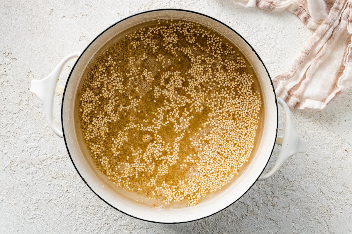 A large white pot filled with water and quinoa while the water is starting to simmer.