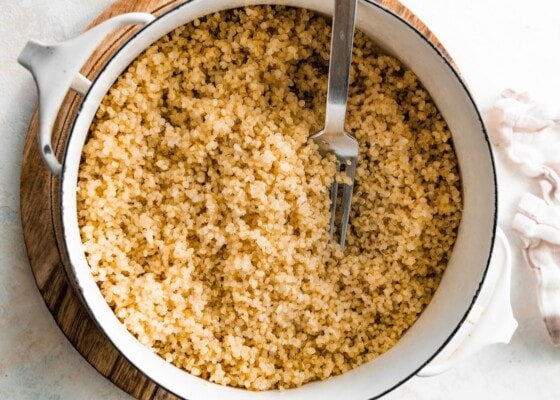 A large white pot filled with cooked quinoa. There is a silver fork in the pot.