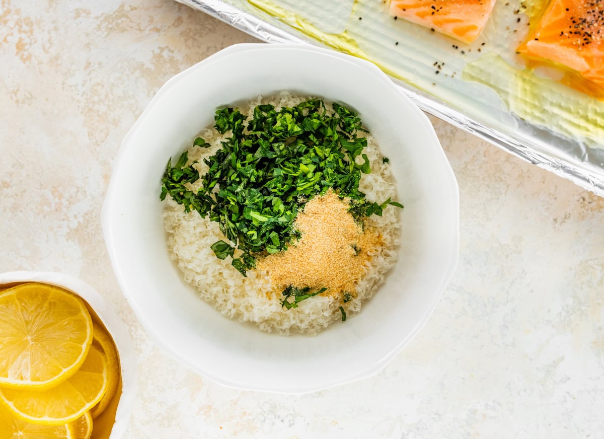 A parmesan herb mixture combined in a small white bowl: parmesan, garlic powder and fresh herbs.