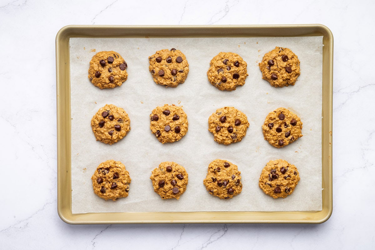 Twelve peanut butter oatmeal cookies on a baking tray after being baked.
