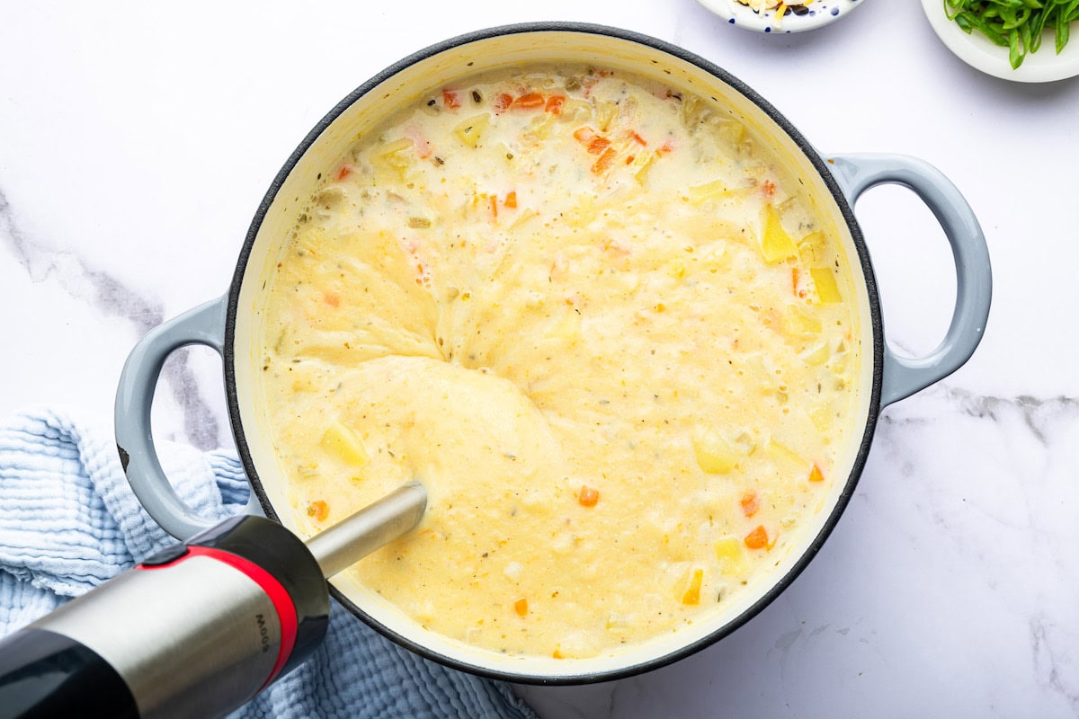 An immersion blender blending the potato soup in a large dutch oven pot.