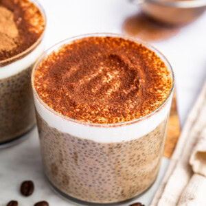 A glass cup of tiramisu chia pudding topped with cocoa powder.