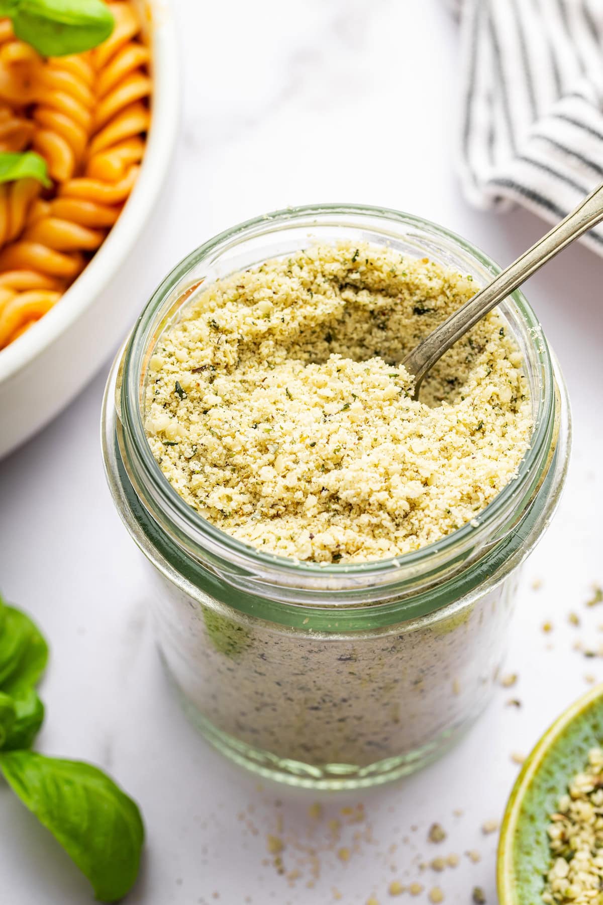 A vegan parmesan cheese made with hemp seeds in a glass mason jar with a metal spoon.