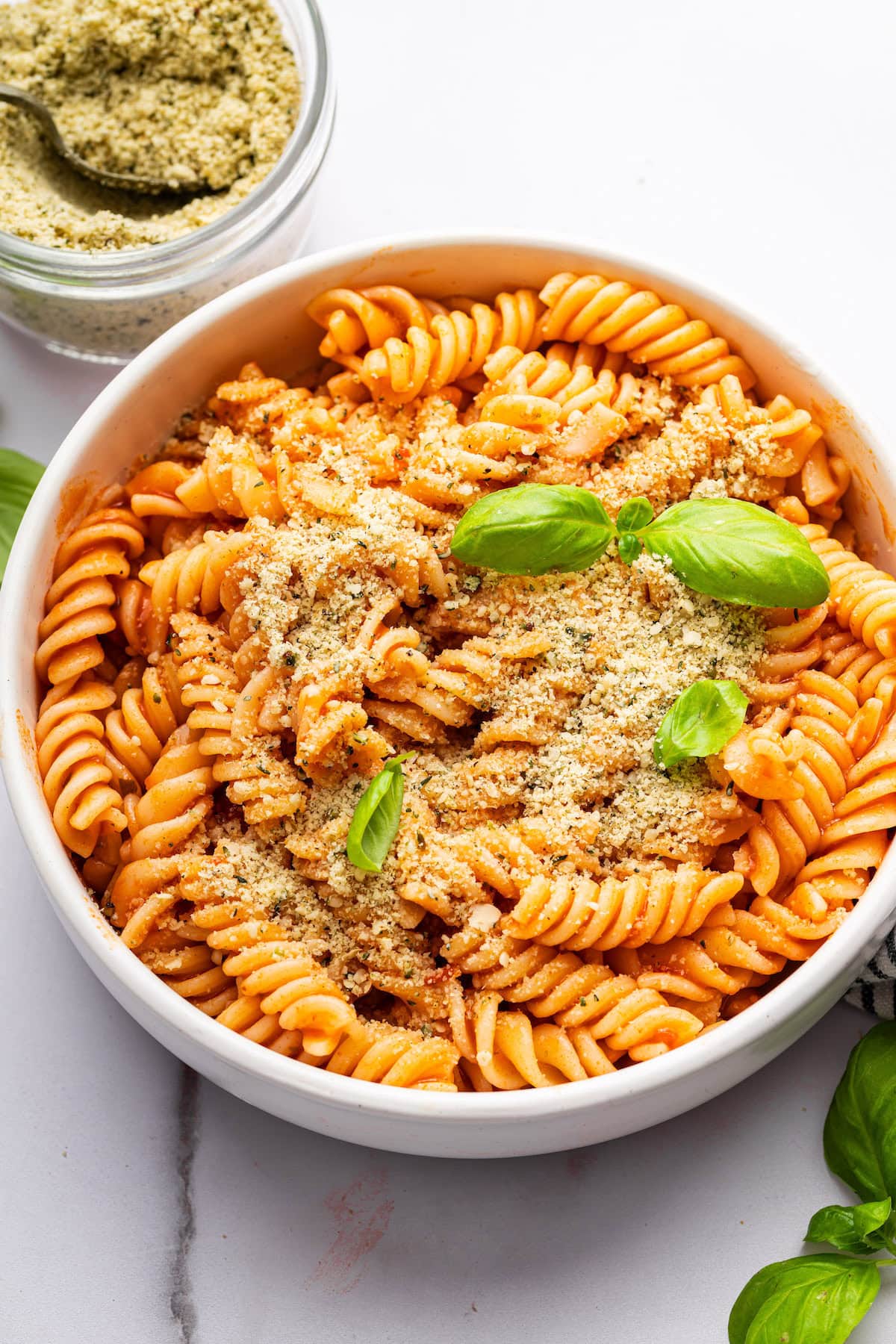 A bowl of pasta garnished with fresh basil and vegan parmesan cheese that is made with hemp seeds.