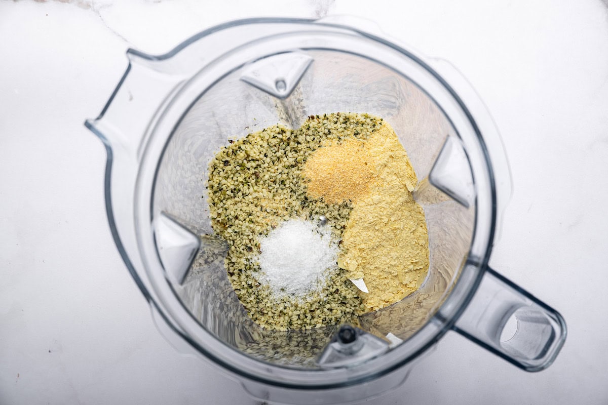 A blender with hemp seeds, nutritional yeast, salt, and garlic powder which will be used to make vegan parmesan cheese.