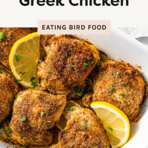 Greek Chicken in a dish with lemons on top.