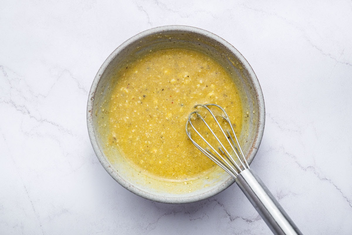 A small bowl of lemon vinaigrette with minced garlic and herbs being whisked together.
