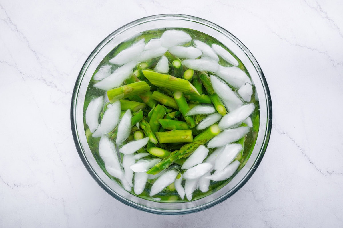 Chopped asparagus in a bowl of ice water, showing the blanching process to preserve color and crispness.